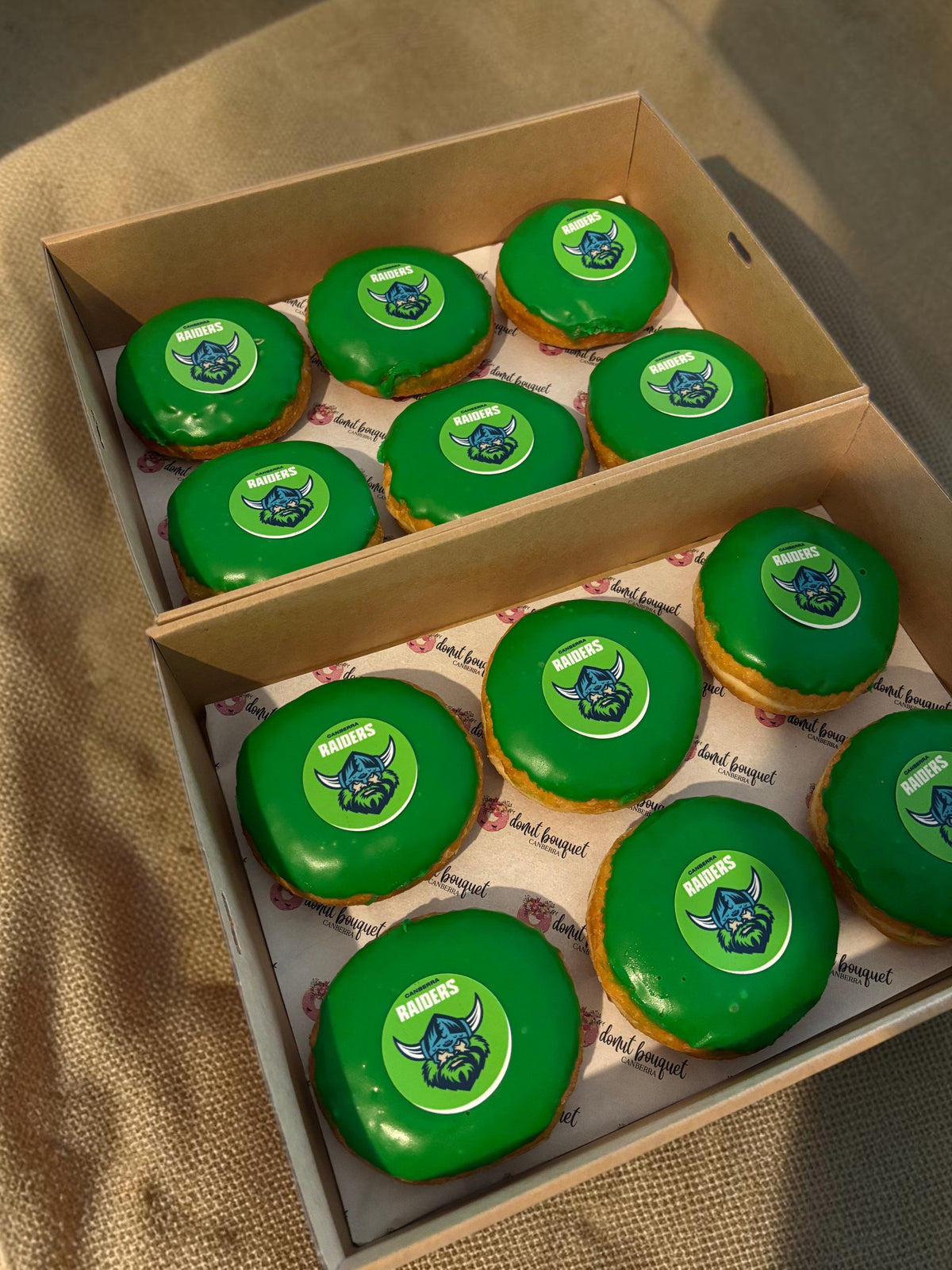 Donut Bouquet Canberra green glazed donuts arranged in rows inside cardboard boxes for a Raiders themed celebration.